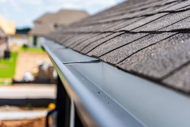 Roof edge with asphalt shingles and seamless aluminum gutter, showcasing quality roofing and water management solutions by Anvil Roofers.